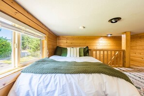 Un dormitorio de cabaña de madera con cama, ventana y barandilla de madera.