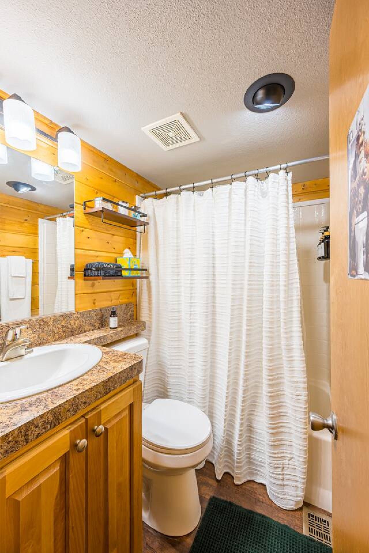 Un baño con tocador de madera, lavamanos, inodoro y cortina de ducha.
