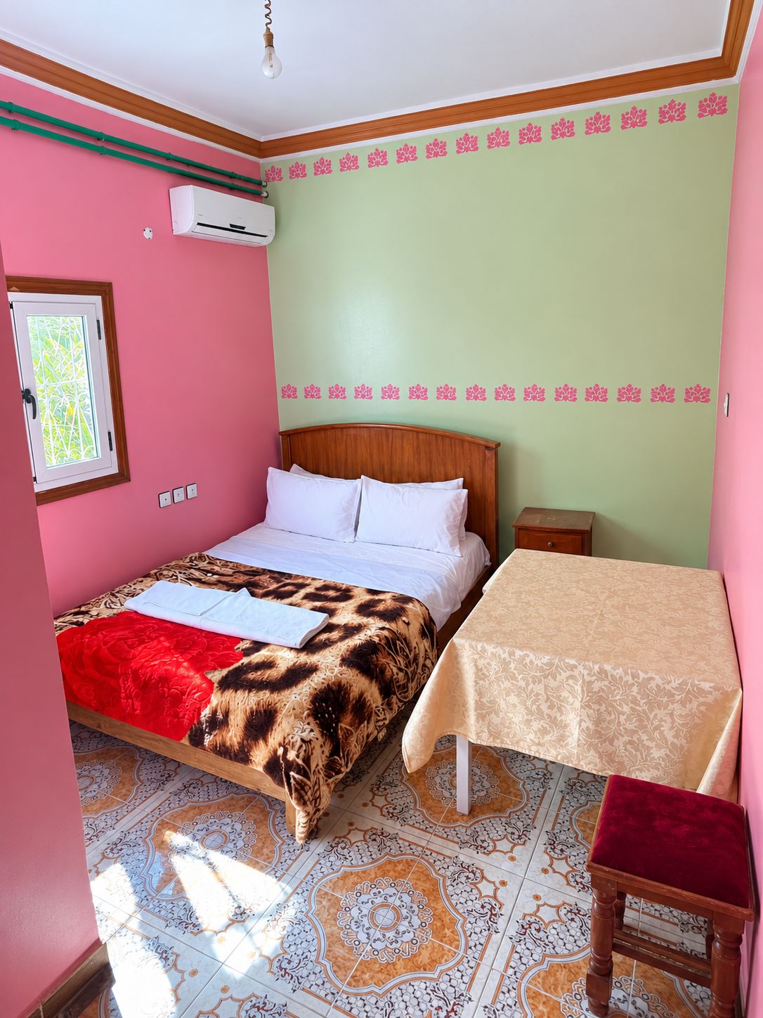 A bedroom with a bed, a bedside table, a chair, a window, and a patterned floor.
