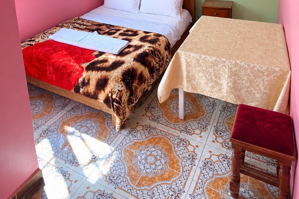 A bedroom with a bed, a bedside table, a chair, a window, and a patterned floor.