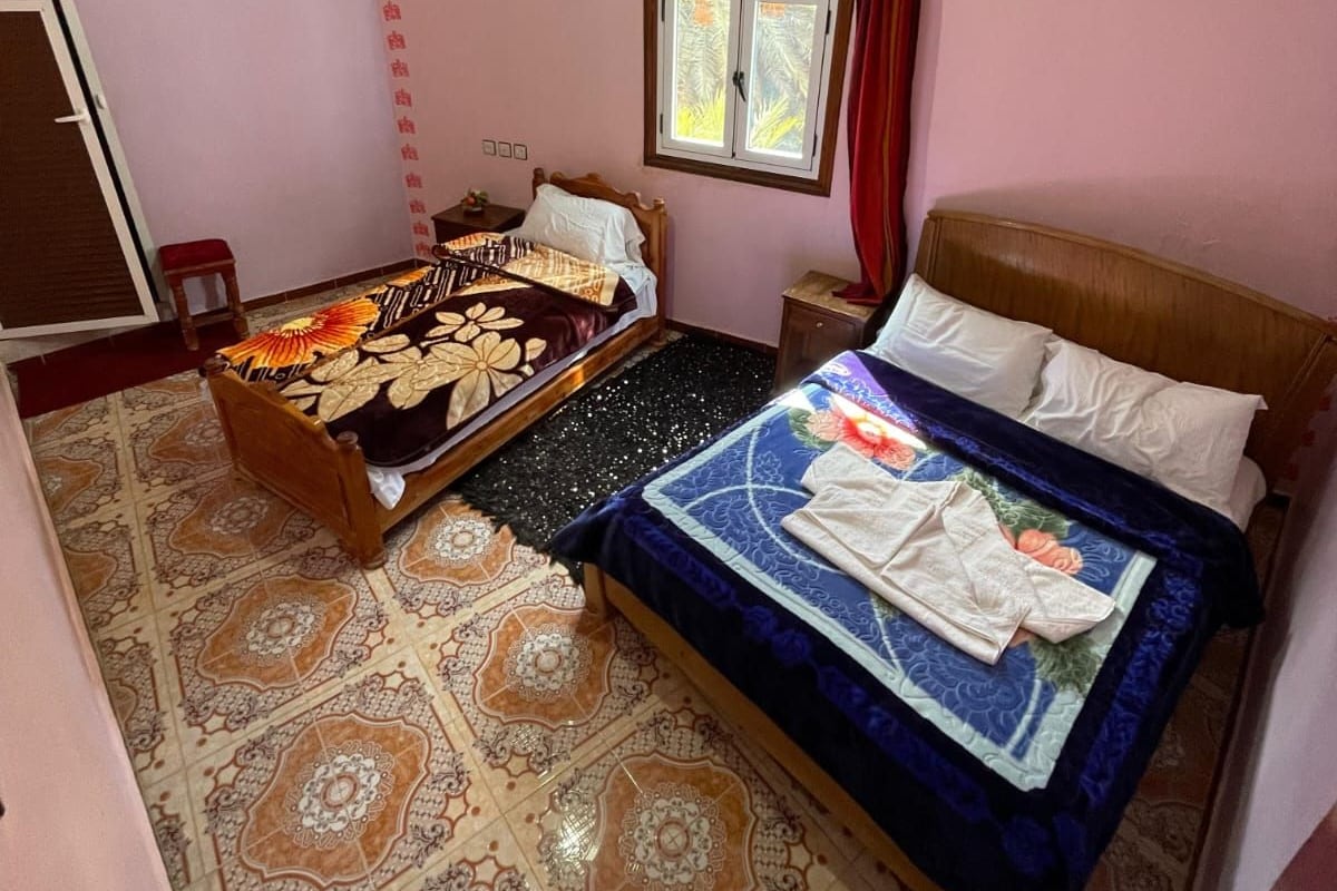 A bedroom with two beds, a window with curtains, a ceiling fan, and patterned floor tiles.