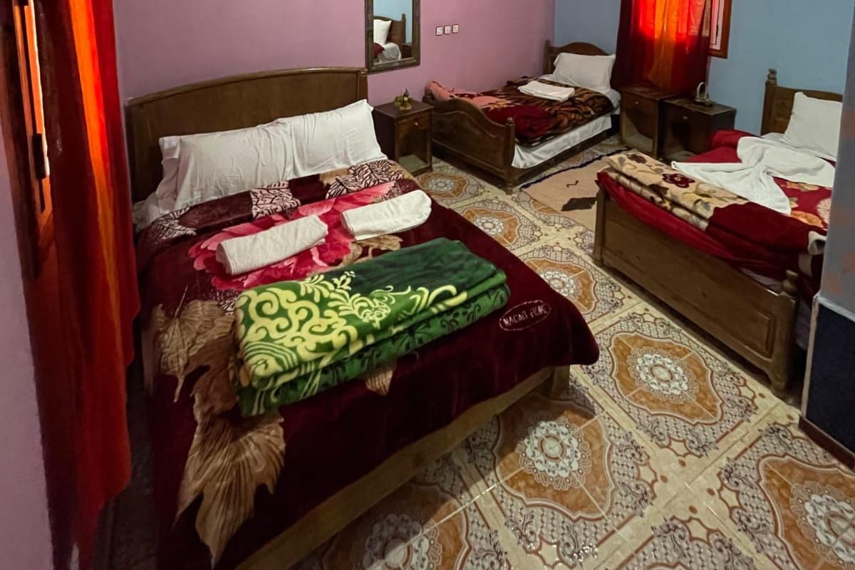 A bedroom with two beds, a ceiling fan, a mirror, and patterned floor tiles.