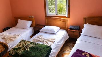 A room with two single beds, a window with a view of greenery, a wooden headboard, and a small bedside table with a lamp.