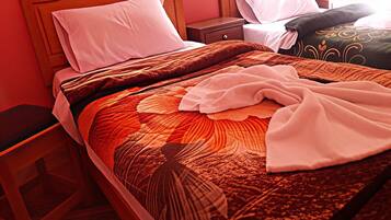 Habitación de hotel con estructura de cama de madera, colcha grande con estampado de hojas y mesita de noche con lámpara.
