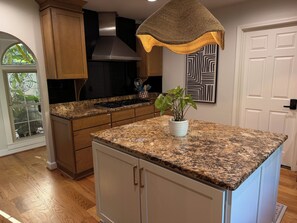 Une cuisine dotée de plans de travail en granit, d’armoires en bois, d’une hotte de cuisinière en acier inoxydable et d’un luminaire suspendu.