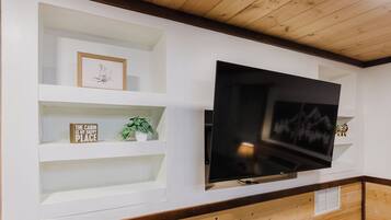 A wall-mounted TV with built-in shelving, a framed picture, and a potted plant.