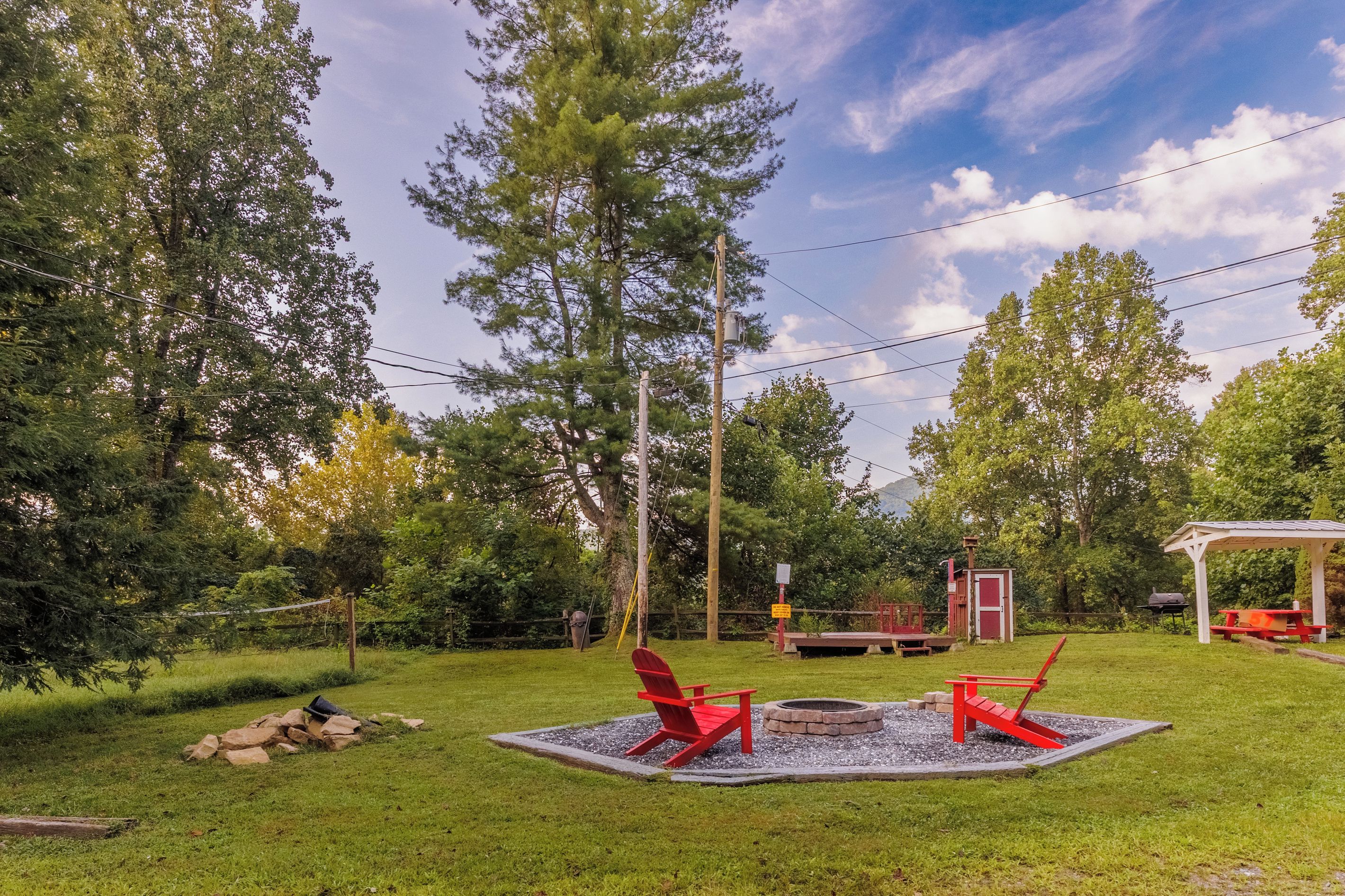 A backyard with a fire pit, red chairs, a wooden deck, and a small shed.