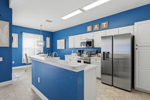 A modern kitchen with blue walls, white cabinetry, and stainless steel appliances. - Themed 5BR Pool & Spa Home + Game Room | Gated Windsor Hills, 4 mi to Disney (Kissimmee)