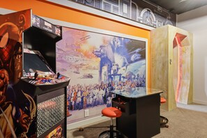 Zona de juegos con máquinas de arcade, un gran mural y asientos.