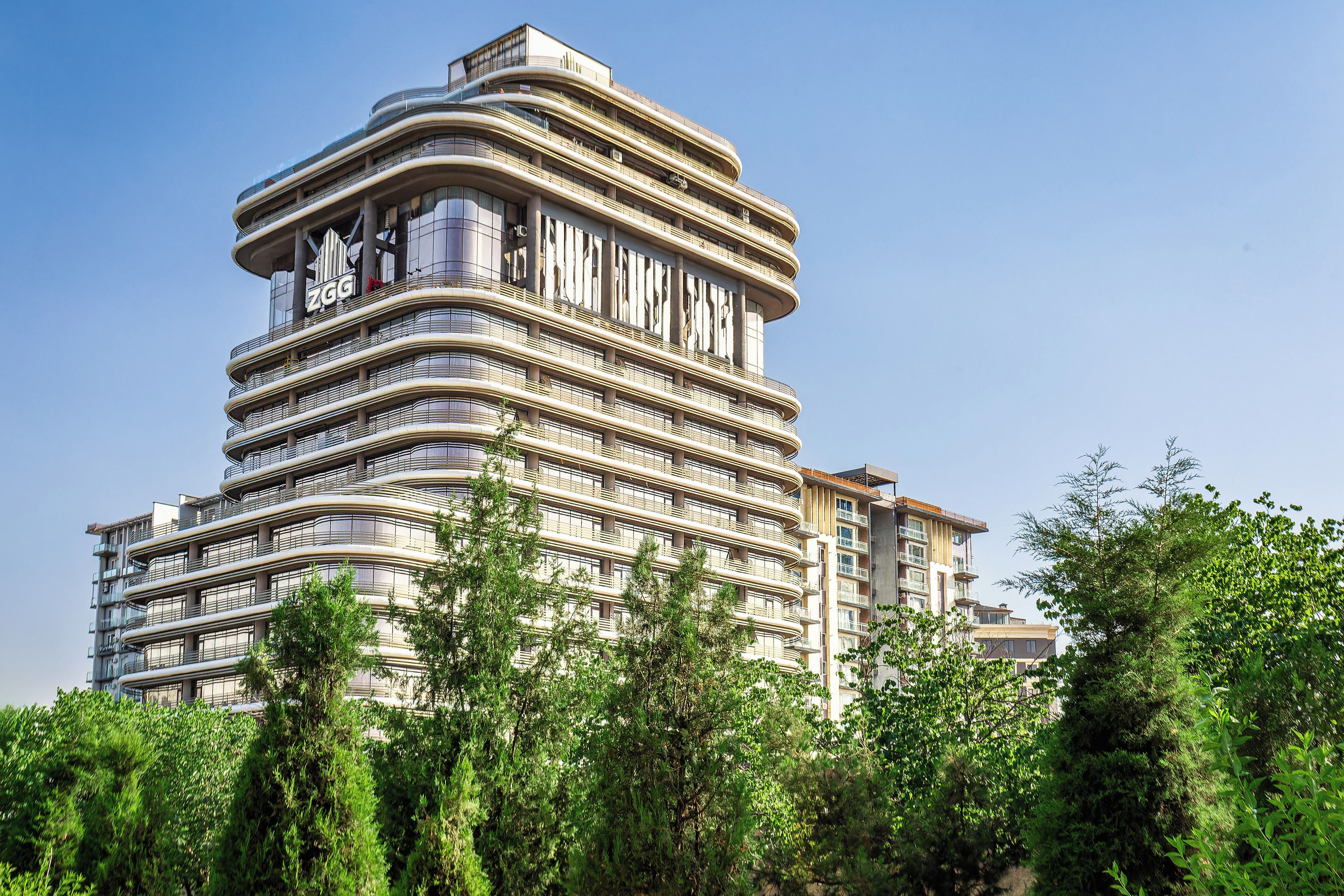 Un immeuble à étages doté d’une architecture originale aux lignes courbes, avec des balcons et un logo bien visible sur la façade.