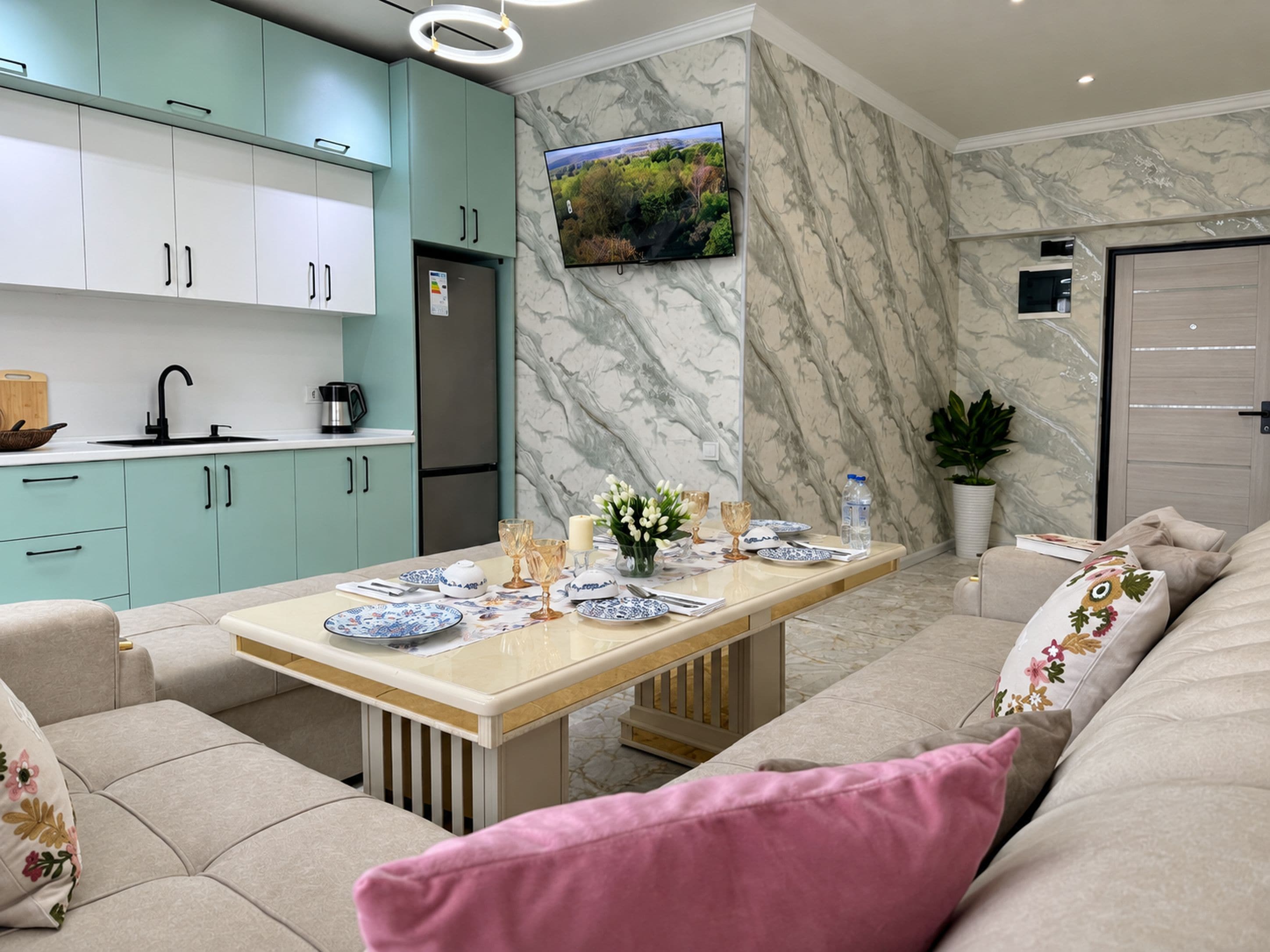 Una sala moderna con un sofá, una mesa de comedor con platos, y una cocina con armarios y un refrigerador.