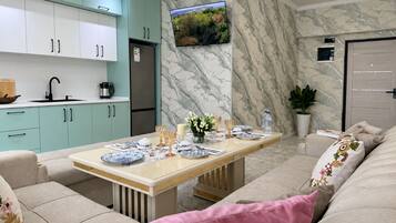 Una sala moderna con un sofá, una mesa de comedor con platos, y una cocina con armarios y un refrigerador.