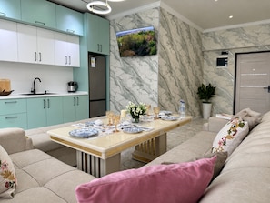 Una sala moderna con un sofá, una mesa de comedor con platos, y una cocina con armarios y un refrigerador.
