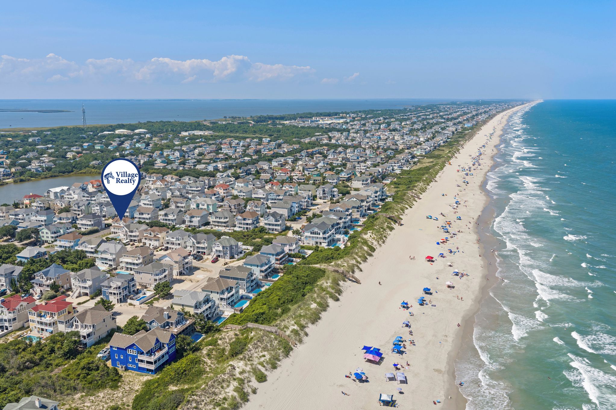 An aerial view of a coastal residential area with houses, a beach, and a lighthouse.