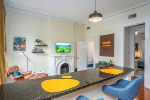 A modern living room with a fireplace, a television, and a bar area with blue chairs. - Sunlit Downtown OTR 1BR Walkable In-Unit Laundry (Cincinnati)