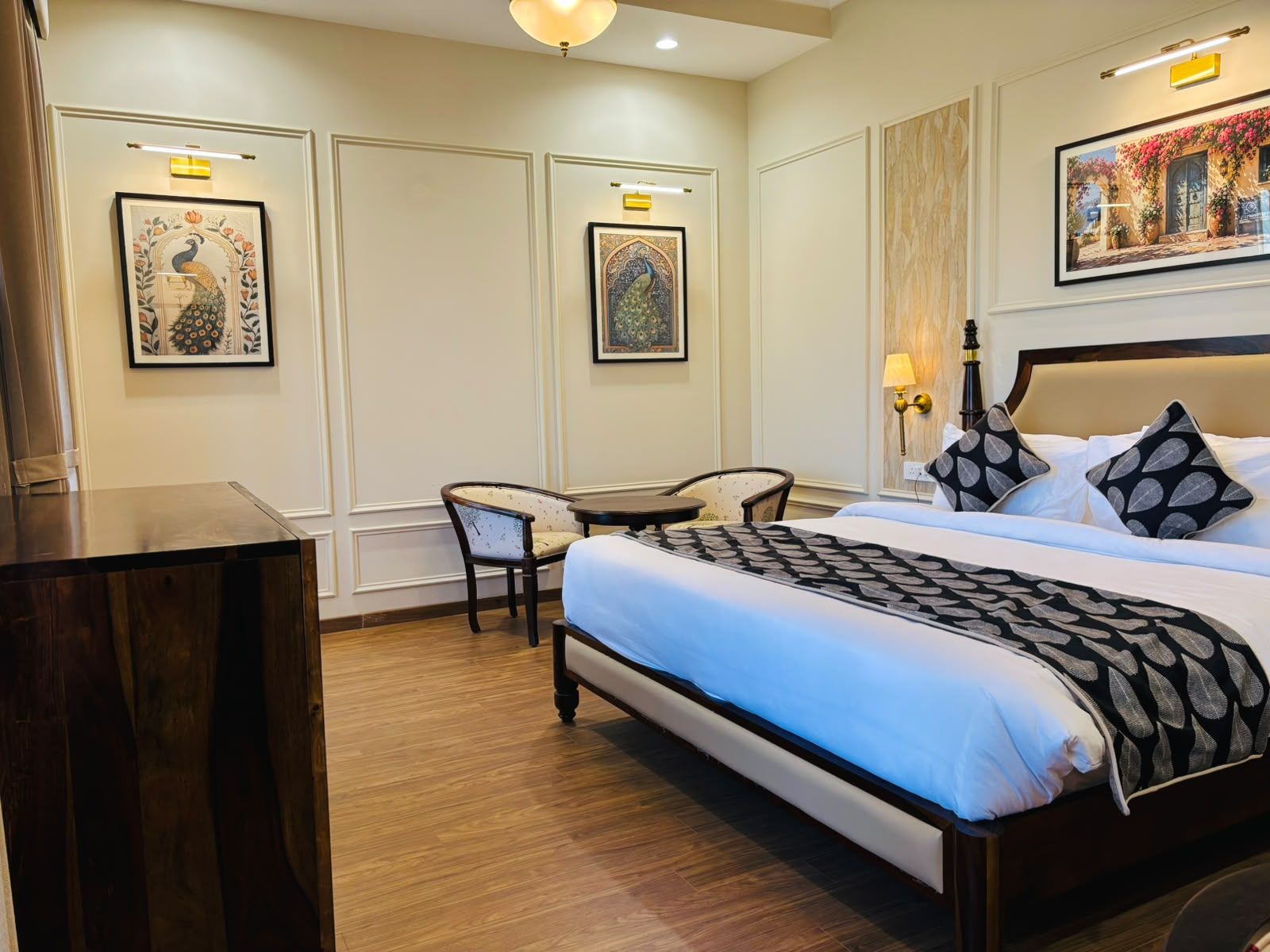 Una habitación de hotel con una cama grande, un escritorio, dos sillas y obras de arte en las paredes.