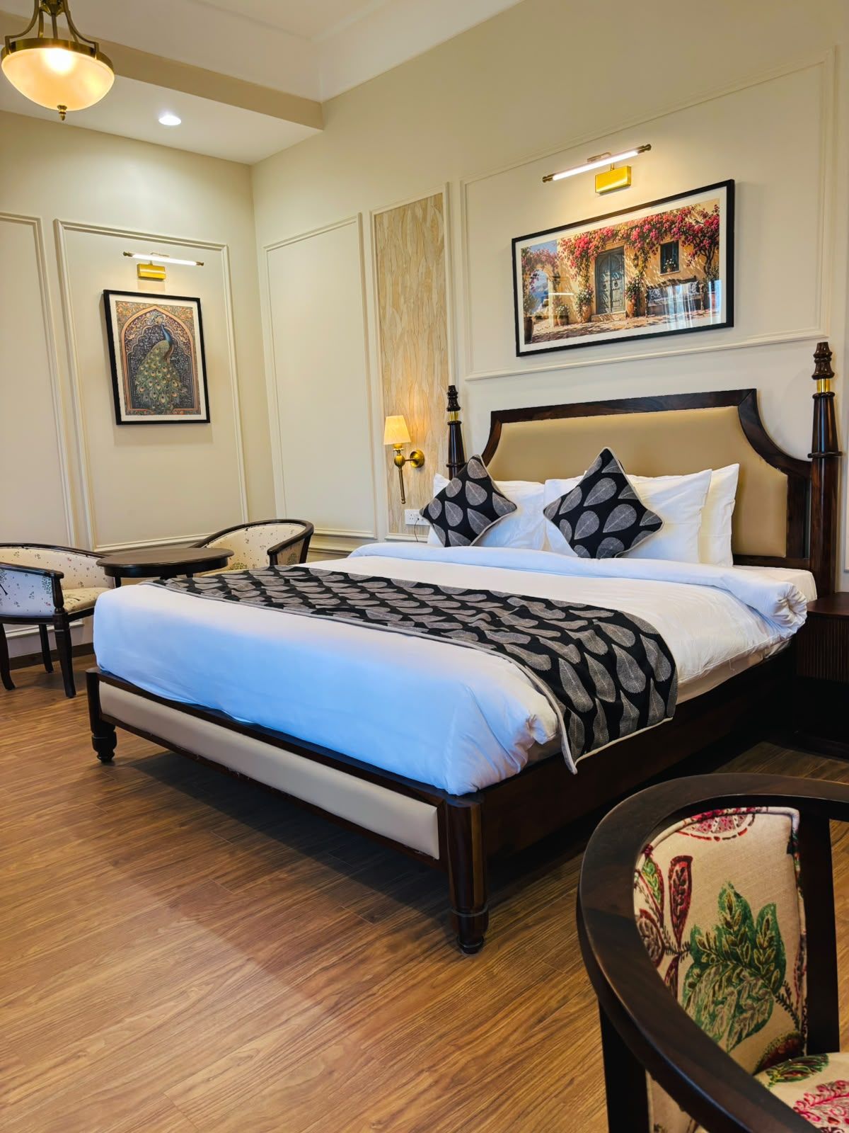Habitación de hotel con una cama grande, una mesita de noche, una silla, una lámpara de pared y un cuadro enmarcado.