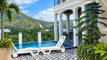 A rooftop pool area with lounge chairs, a patterned floor, and a view of a mountain.