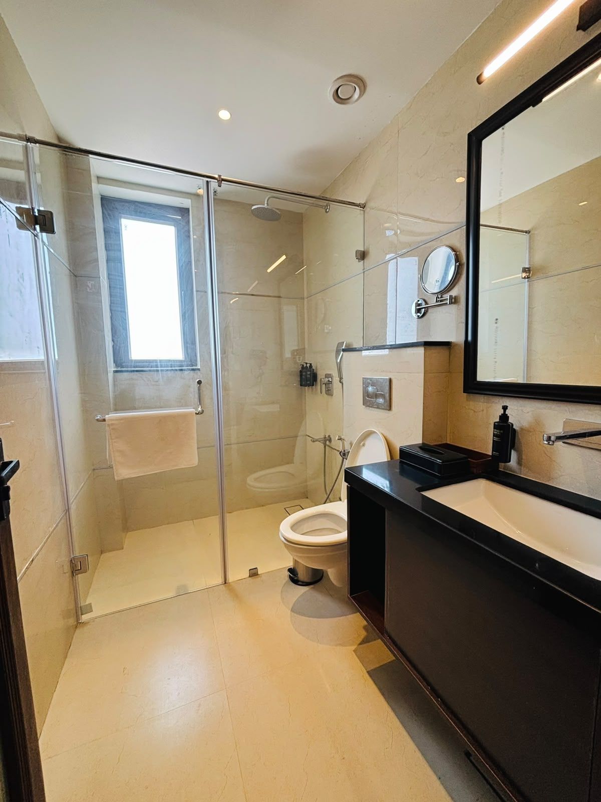 Un baño moderno con ducha envuelta en vidrio, inodoro y tocador con un espejo grande.