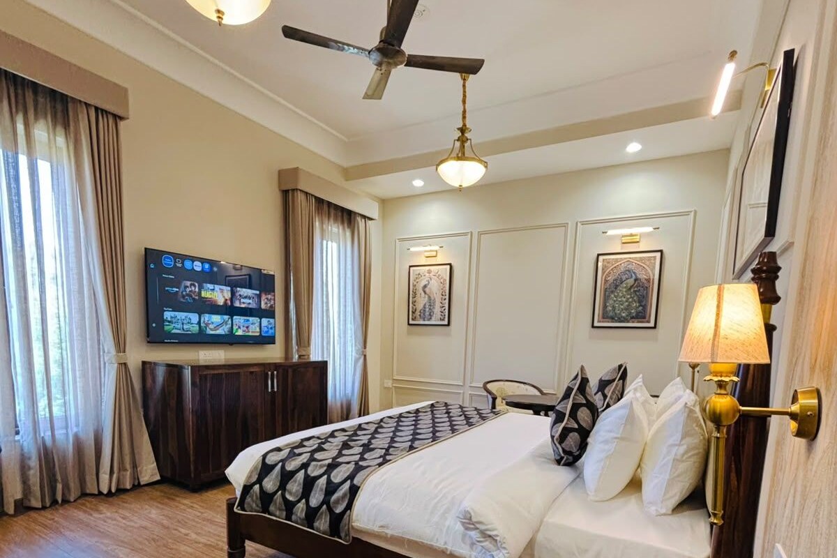 A hotel room with a bed, a television, a ceiling fan, and artwork on the walls.