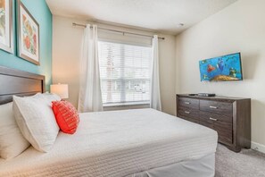 A bedroom with a bed, a dresser, a window with curtains, and a wall-mounted TV. - Serenity 3BR Townhome w/ Private Pool (Clermont)