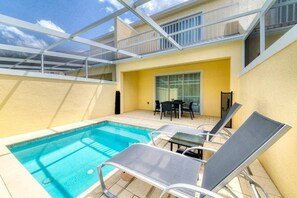 Piscina com espreguiçadeiras, mesa e porta de vidro que dá para uma área externa.