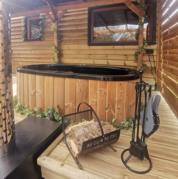 A rustic wooden cabin with a hot tub, a fireplace, and a wooden table with a sign reading 'AU COIN DU FED'.