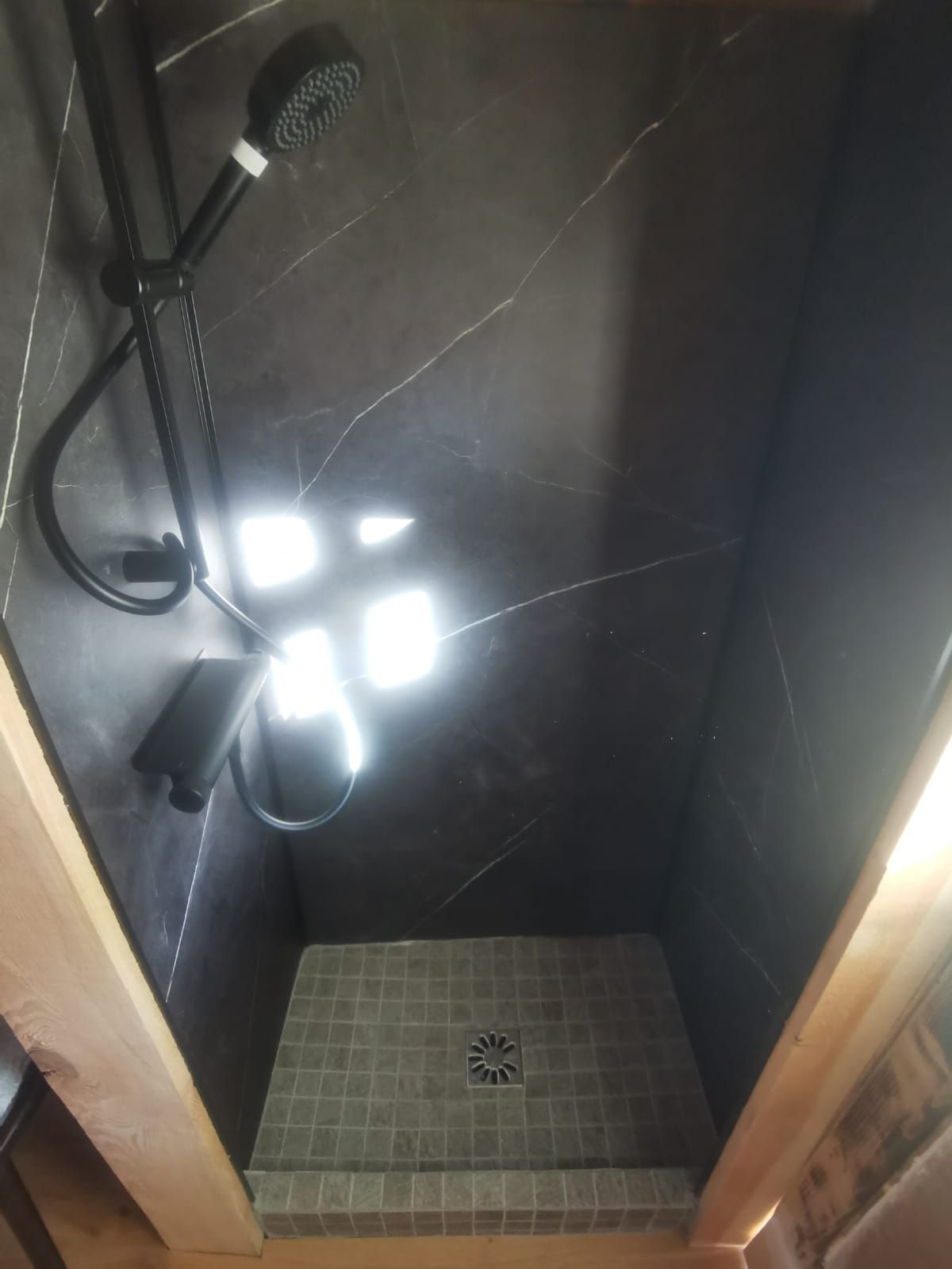 A small, dark-colored shower stall with a handheld showerhead and a wall-mounted faucet.