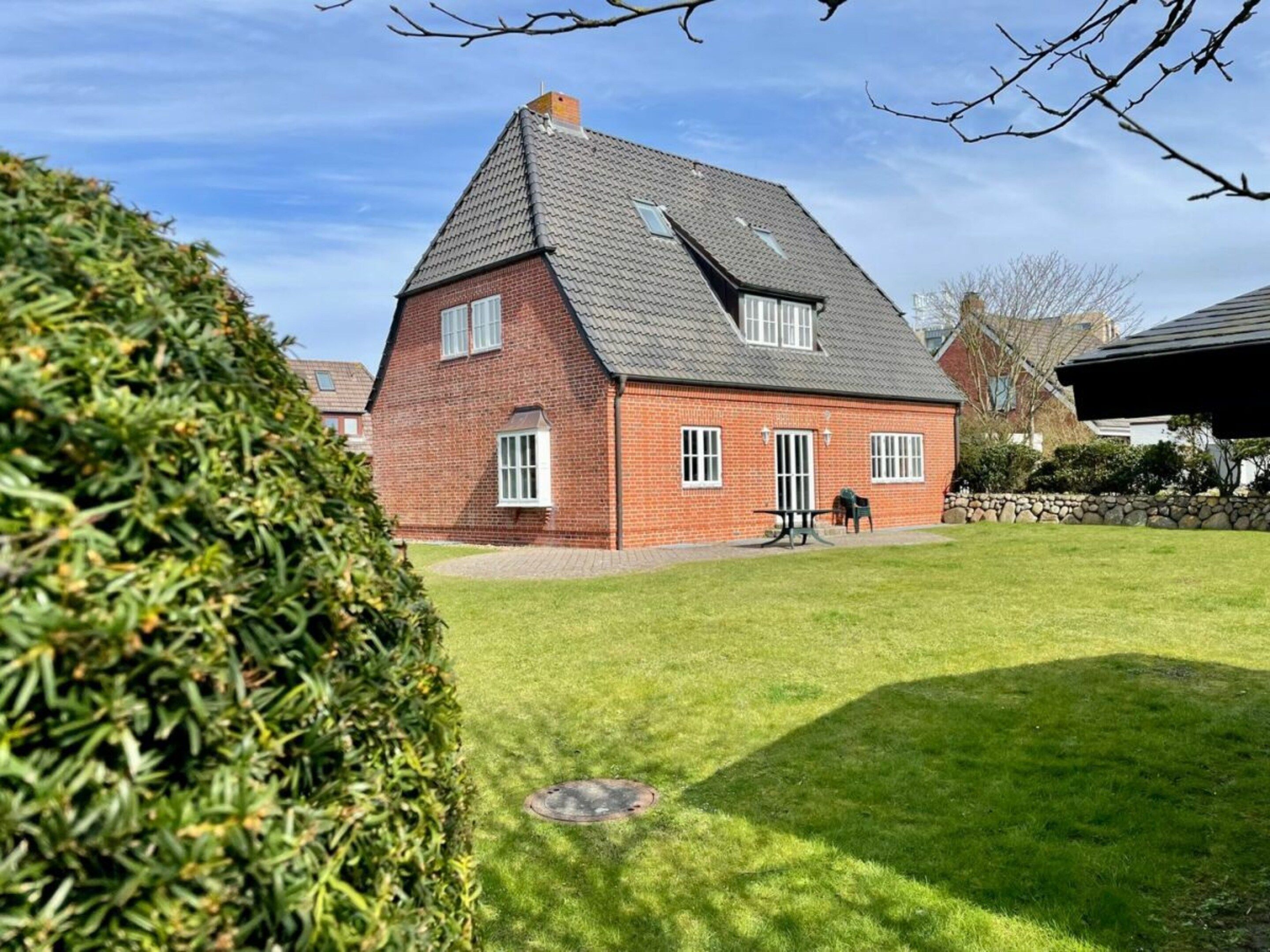 A brick house with a sloped roof, a well-maintained lawn, and a stone wall in the background.