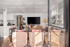 Un salon moderne avec un téléviseur à écran plat, un coin repas agrémenté d’un vase de fleurs et une cuisine en arrière-plan.