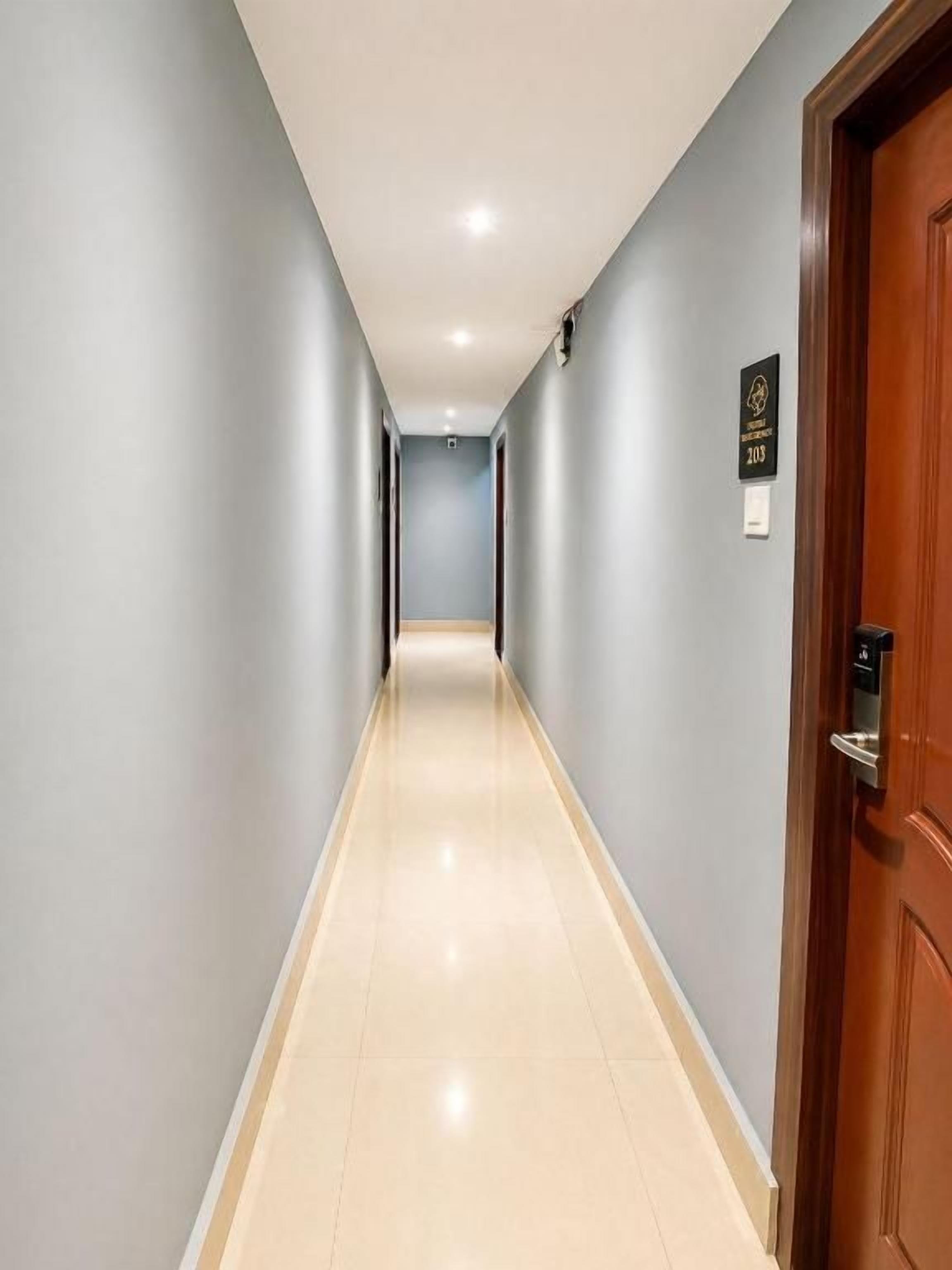 A hallway with a wooden door on the right, a sign above it, and a light-colored floor.