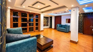 A spacious living area with a wooden floor, a blue sofa, a coffee table, and a large window.
