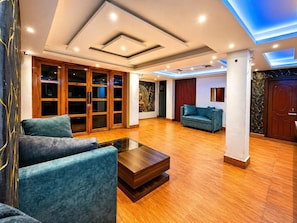 A spacious living area with a wooden floor, a blue sofa, a coffee table, and a large window. - The Royal Sheep Residency (Gangtok)