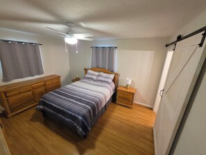 Ein Schlafzimmer mit Bett, einem Holzschrank, einem Nachttisch und einem Deckenventilator.