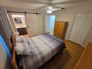 A bedroom with a bed, a wardrobe, a ceiling fan, and a bathroom visible through an open door. - 2-bedroom quaint pool house in Ocala with cool AC. (Ocala)