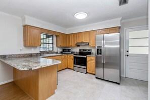 A kitchen with wooden cabinets, a stainless steel refrigerator, a microwave, and an oven. - 2-bedroom quaint pool house in Ocala with cool AC. (Ocala)