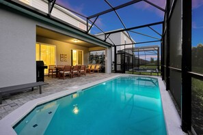 A swimming pool with a glass enclosure, wooden furniture, and a view of the outdoors. - Windsor Cay 5BR • Pool, Themed Rooms, Lazy River (Clermont)