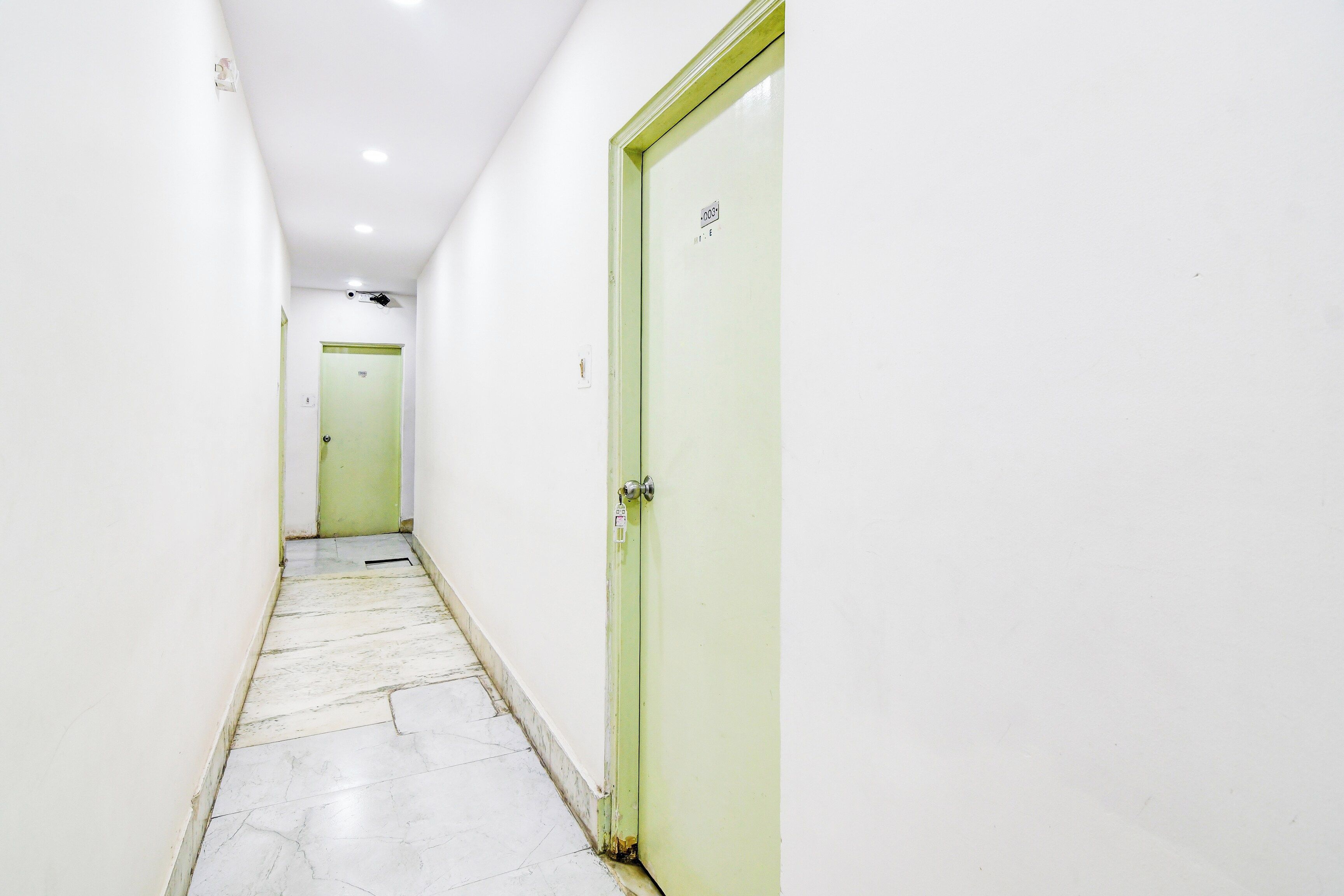 Un pasillo estrecho con paredes blancas y una puerta verde a la derecha.