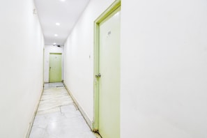 Corredor estreito com paredes brancas e uma porta verde à direita.