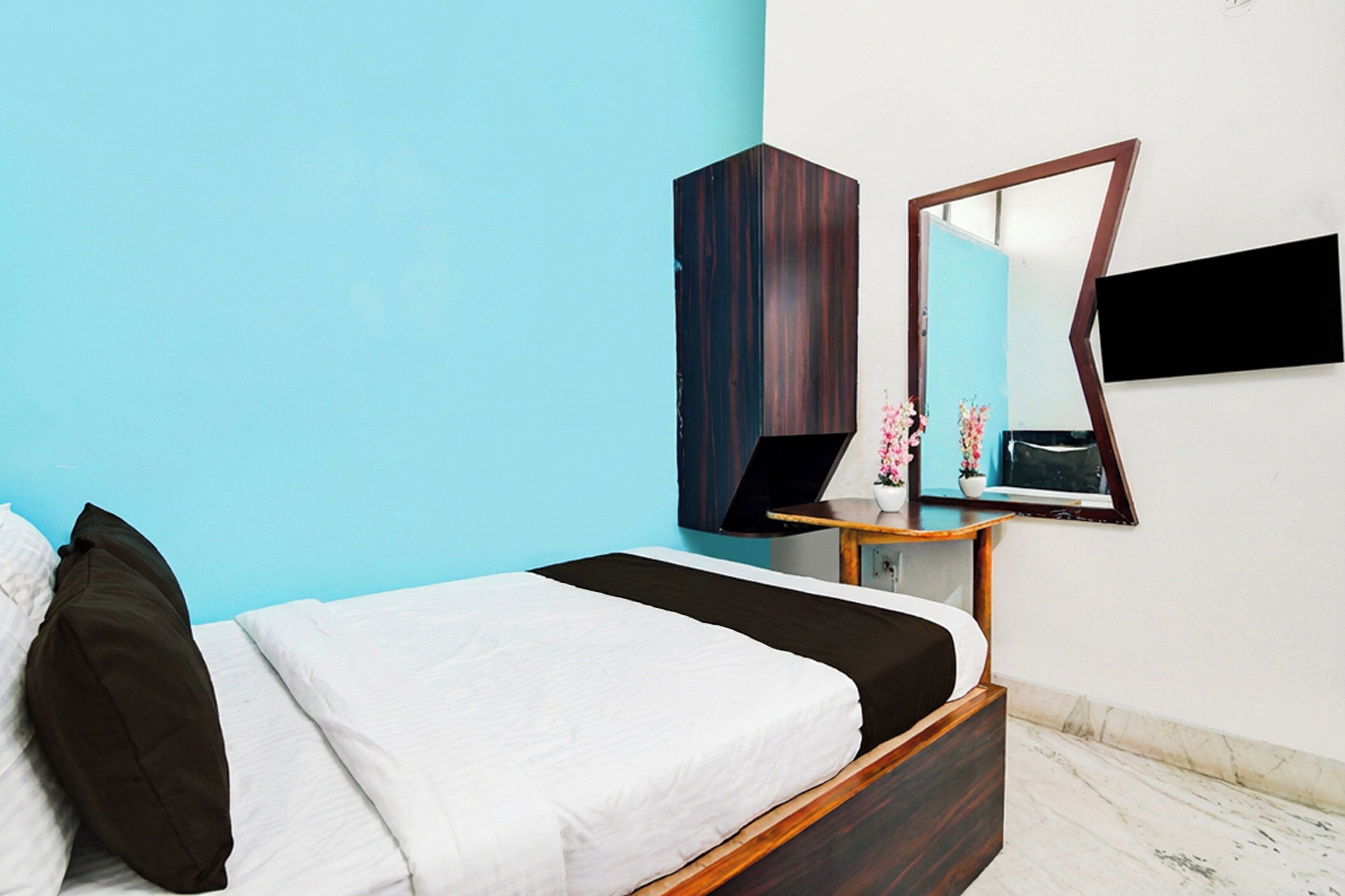 Un dormitorio con cama, cómoda, espejo y una pequeña mesa con flores.