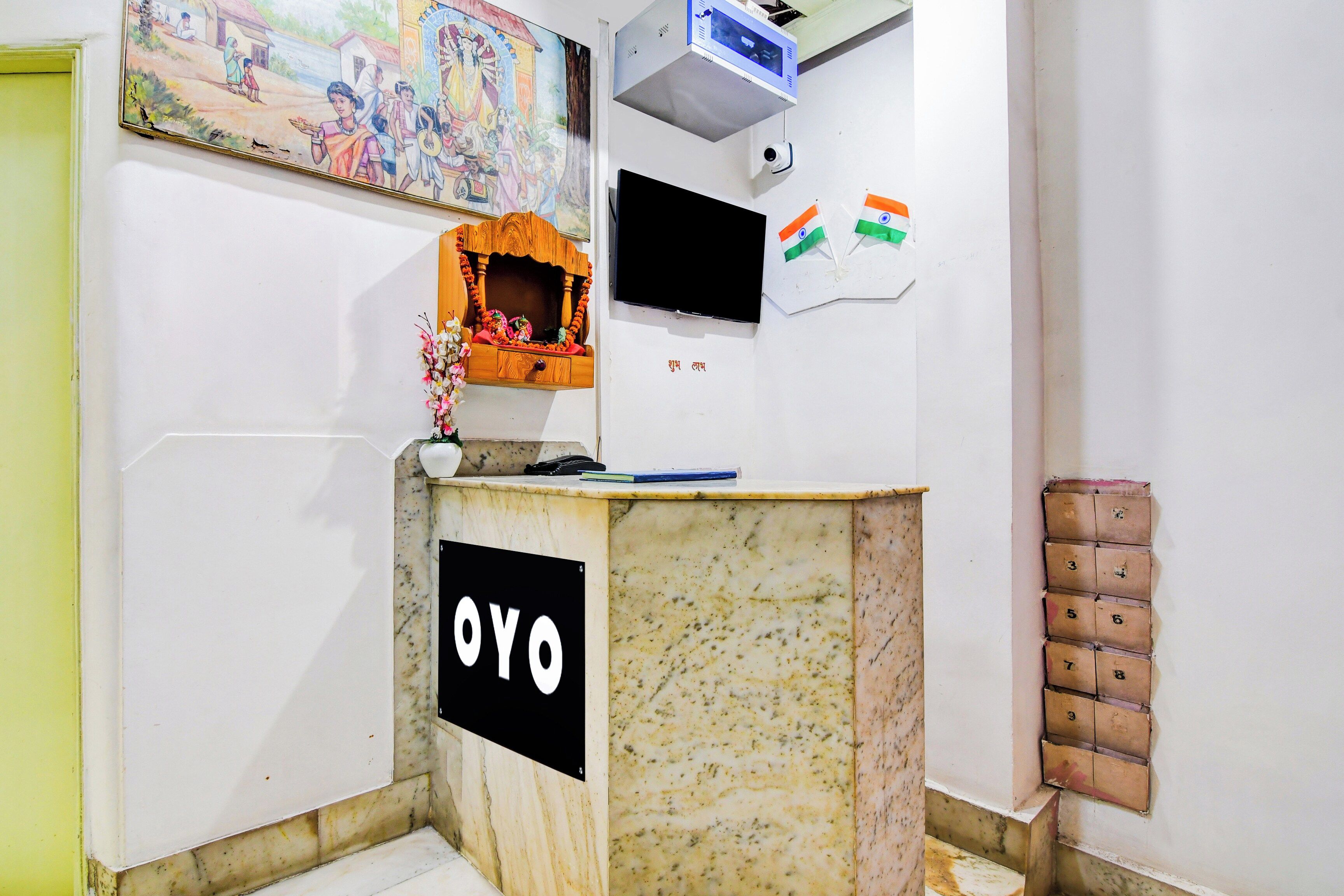 Una recepción con un letrero que dice 'OYO', una cámara de seguridad y un televisor montado en la pared.