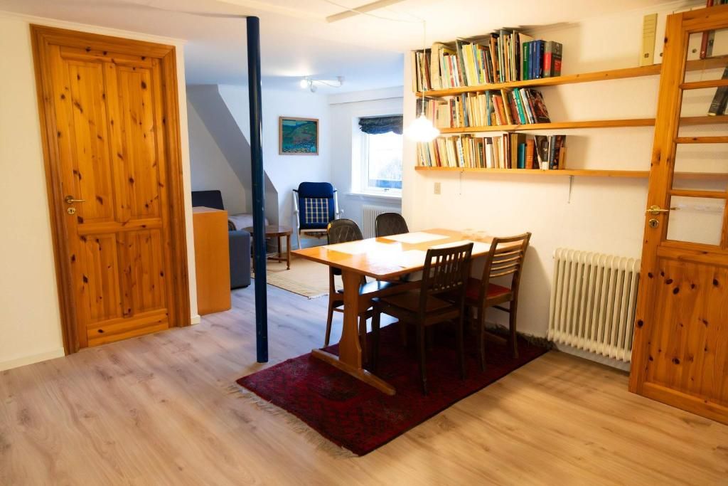 A room with a wooden table and chairs, a bookshelf, and a radiator.