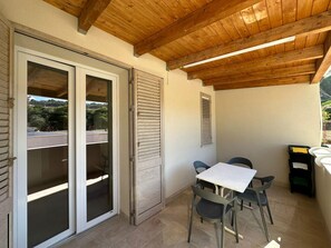 A covered patio with a table and chairs, a sliding glass door, and a window with shutters. - New Listing (Balestrate)
