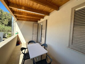 A covered outdoor seating area with a table and chairs, a window with shutters, and a view of greenery. - New Listing (Balestrate)