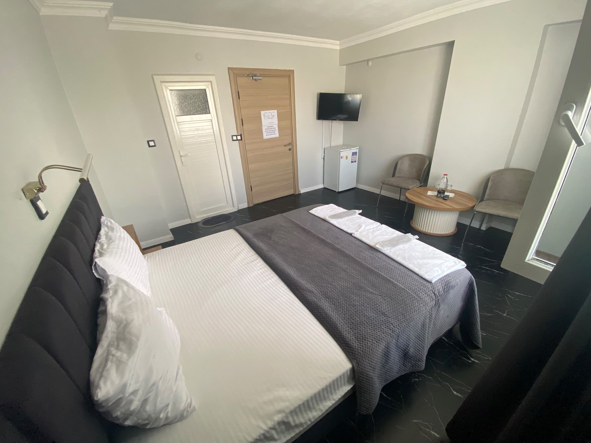 A hotel room with a bed, a chair, a small table, a television, and a door.