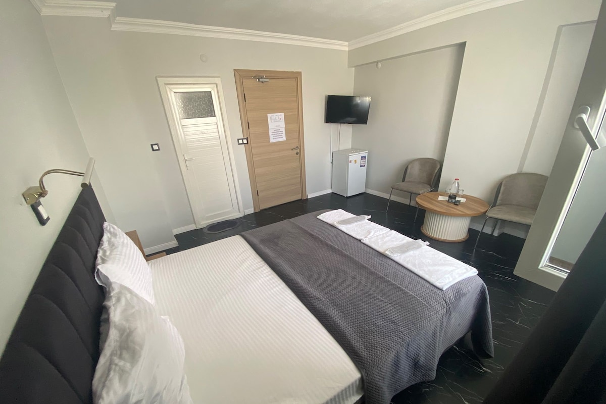 A hotel room with a bed, a chair, a small table, a television, and a door.