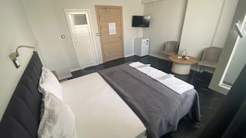A hotel room with a bed, a chair, a small table, a television, and a door.