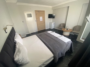 A hotel room with a bed, a chair, a small table, a television, and a door. - Şelale Apart Otel (Afyonkarahisar)