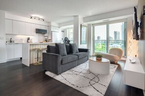 A modern living room with a grey sofa, a round coffee table, and a white rug. - Lakefront Oasis Modern 1BR w Den (Toronto)