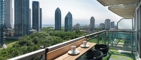 A balcony with a table and chairs, overlooking a cityscape with tall buildings and greenery.